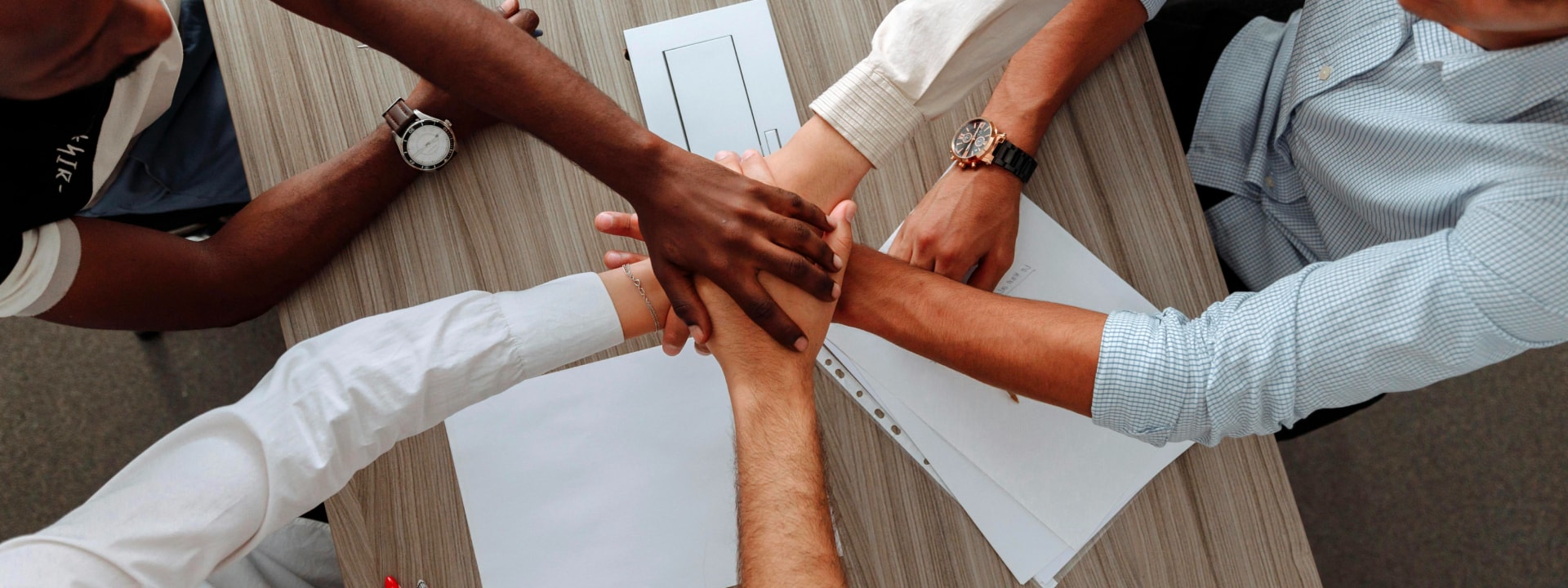 Group of diverse hands joined together over a table, symbolizing teamwork, unity, and collaboration, representing Solavita's commitment to strong partnerships and cooperative sales efforts