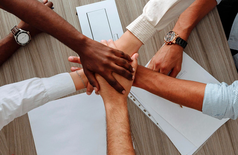 Group of diverse hands joined together over a table, symbolizing teamwork, unity, and collaboration, representing Solavita's commitment to strong partnerships and cooperative sales efforts